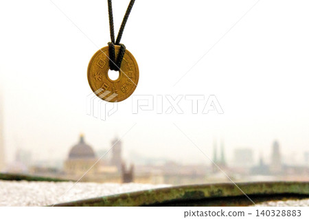 Lucky japanese 5 yen coin necklace displayed with a blurred foggy Berlin skyline in the background, symbolizing good fortune and cultural heritage. Selective focus. Copy space Lucky japanese 5 yen coin necklace displayed with a blurred foggy Berlin skyline in the background, symbolizing good fortune and cultural heritage. Selective focus. Copy space 140328883