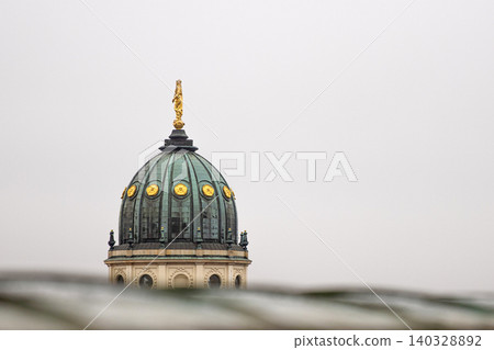 Closeup of the New German Cathedral Dome. Iconic Berlin landmark with golden statue details, seen from the French Church rooftop terrace against a soft skyline.  Minimalist photo. Copy space 140328892