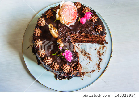 Top view of luxurious chocolate layer cake decorated with roses and intricate details, partially eaten. Glass plate with birthday cake with floral decorations and a slice removed. Copy space Top view of luxurious chocolate layer cake decorated with roses and intricate details, partially eaten. Glass plate with birthday cake with floral decorations and a slice removed. Copy space 140328934