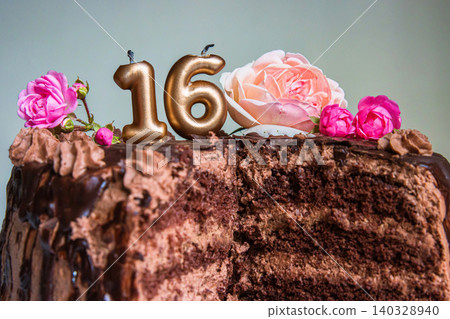 Sweet sixteen chocolate birthday cake decorated with golden glowing lit 16 candles and pink roses. Handmade torte for celebration of a special milestone event. Card design. Selective focus. Copy space Sweet sixteen chocolate birthday cake decorated with golden glowing lit 16 candles and pink roses. Handmade torte for celebration of a special milestone event. Card design. Selective focus. Copy space 140328940