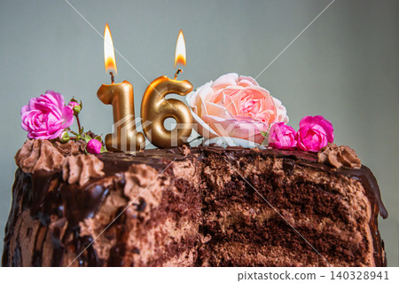 Sweet sixteen chocolate birthday cake decorated with golden glowing lit 16 candles and pink roses. Handmade torte for celebration of a special milestone event. Card design. Selective focus. Copy space Sweet sixteen chocolate birthday cake decorated with golden glowing lit 16 candles and pink roses. Handmade torte for celebration of a special milestone event. Card design. Selective focus. Copy space 140328941