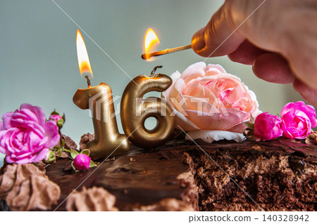 Closeup of a womans hand lighting golden 16 candles on a chocolate birthday cake decorated with pink and peach roses for a sweet sixteen celebration Closeup of a womans hand lighting golden 16 candles on a chocolate birthday cake decorated with pink and peach roses for a sweet sixteen celebration 140328942