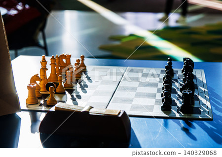 Chessboard with wooden pieces on a blue table, arranged for a new game on a tournament board, symbolizing intelligence, competition, and classic board game tactics. Selective focus Chessboard with wooden pieces on a blue table, arranged for a new game on a tournament board, symbolizing intelligence, competition, and classic board game tactics. Selective focus 140329068