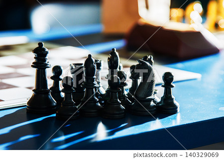 Black chess pieces on a blue table with sunlight and shadows. Closeup of dark chess in dramatic lighting, symbolizing intelligence, planning and contrast between light and shadow. Selective focus Black chess pieces on a blue table with sunlight and shadows. Closeup of dark chess in dramatic lighting, symbolizing intelligence, planning and contrast between light and shadow. Selective focus 140329069