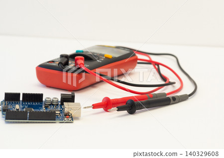 A multimeter with test probes and a circuit board lie on a white background. 140329608