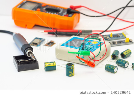 A multimeter with test probes, a soldering iron, and tools lie on a white background. A multimeter with test probes, a soldering iron, and tools lie on a white background. 140329641