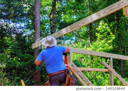 Worker climbs ladder to install beams for wooden project in construction works zone Worker climbs ladder to install beams for wooden project in construction works zone 140329644
