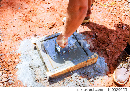 Worker install anchor bracket mixes levels cement in wooden frame at construction site Worker install anchor bracket mixes levels cement in wooden frame at construction site 140329655