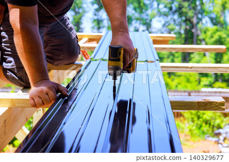 Worker fastens metal sheets to wooden joins beams supports with drill on construction site Worker fastens metal sheets to wooden joins beams supports with drill on construction site 140329677