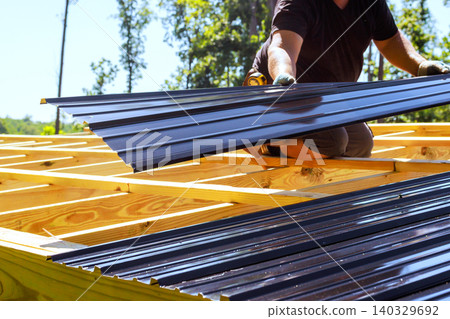 Roofing worker places metal roofing sheets on wooden structure in construction area Roofing worker places metal roofing sheets on wooden structure in construction area 140329692
