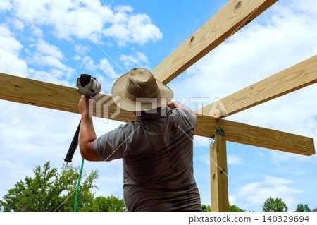 Builder constructs wooden joins beams structure outside under construction day Builder constructs wooden joins beams structure outside under construction day 140329694