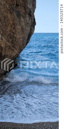 A rocky beach with crystal clear blue water hidden among the rocks 140329714