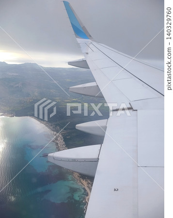 View from the airplane window of the wing, sea and coast on a sunny day View from the airplane window of the wing, sea and coast on a sunny day 140329760
