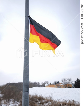 A German flag flutters in the wind against a winter landscape on a bridge. A German flag flutters in the wind against a winter landscape on a bridge. 140329785
