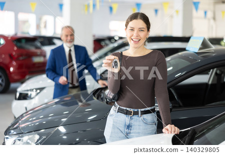 Happy cheerful girl bought car - portrait of joyful girl with car keys in car dealership Happy cheerful girl bought car - portrait of joyful girl with car keys in car dealership 140329805