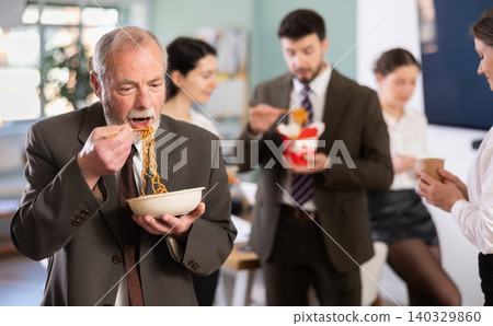 Mature businessman having takeout meal during lunch break at work with other colleagues in office Mature businessman having takeout meal during lunch break at work with other colleagues in office 140329860