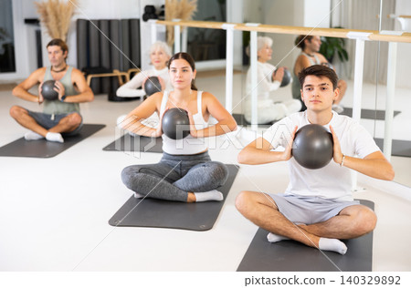 Young man practicing pilates with ball on gray mat in gym room Young man practicing pilates with ball on gray mat in gym room 140329892