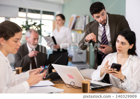 Strict male boss scolding female office worker for scrolling social media on smartphone during work hours in office of business company Strict male boss scolding female office worker for scrolling social media on smartphone during work hours in office of business company 140329909