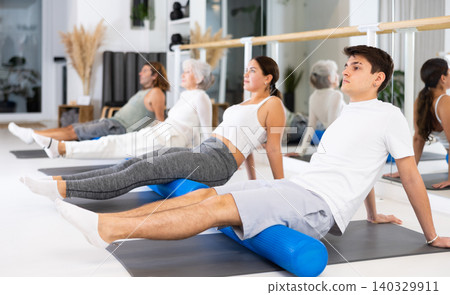 Sports people practicing pilates with rolled mats at group class in yoga studio Sports people practicing pilates with rolled mats at group class in yoga studio 140329911