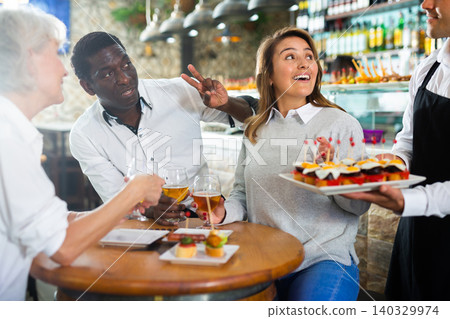 Positive Latin waiter in apron pointing hand on plate with pinchos in the middle of the bar Positive Latin waiter in apron pointing hand on plate with pinchos in the middle of the bar 140329974