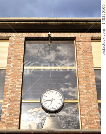 A unique station clock on a pole against the backdrop of a brick building and clouds A unique station clock on a pole against the backdrop of a brick building and clouds 140330106