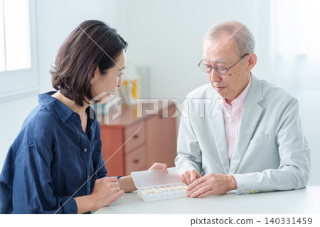 An elderly man receives an explanation about his medication from his daughter. An elderly man receives an explanation about his medication from his daughter. 140331459
