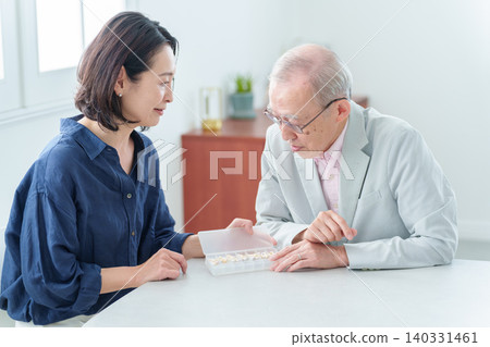 An elderly man receives an explanation about his medication from his daughter. An elderly man receives an explanation about his medication from his daughter. 140331461