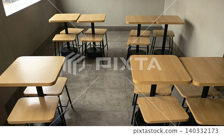 Photo of a modern cafe interior featuring an arrangement of wooden tables and chairs with a minimalist design. Photo of a modern cafe interior featuring an arrangement of wooden tables and chairs with a minimalist design. 140332173
