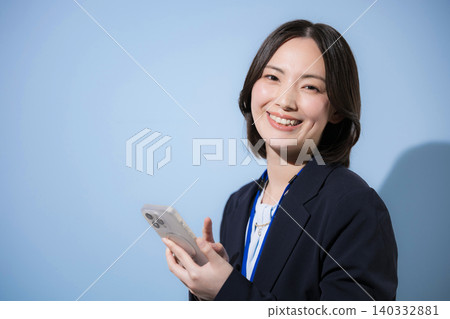 A businesswoman is looking directly at the camera while using her smartphone to search, find, inquire about, and check contacts against a light blue background. A businesswoman is looking directly at the camera while using her smartphone to search, find, inquire about, and check contacts against a light blue background. 140332881