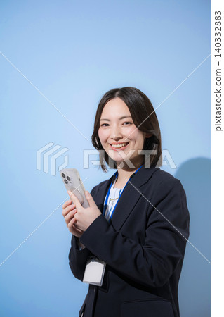 A businesswoman is looking directly at the camera while using her smartphone to search, find, inquire about, and check contacts against a light blue background. A businesswoman is looking directly at the camera while using her smartphone to search, find, inquire about, and check contacts against a light blue background. 140332883