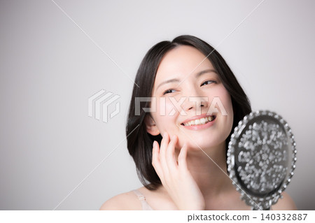 一位年輕女子對著手鏡觸摸自己的皮膚,檢查皮膚狀況,並近距離觀察她的護膚流程。 一位年輕女子對著手鏡觸摸自己的皮膚,檢查皮膚狀況,並近距離觀察她的護膚流程。 140332887