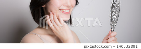 A young woman checks the condition of her skin by touching it while looking in a hand mirror, and the camera zooms in on her skincare routine, but her face is obscured, only her mouth is visible. A young woman checks the condition of her skin by touching it while looking in a hand mirror, and the camera zooms in on her skincare routine, but her face is obscured, only her mouth is visible. 140332891
