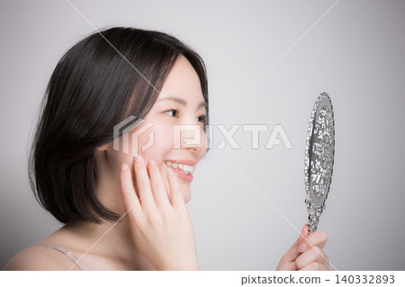A young woman checks the condition of her skin by touching it while looking in a hand mirror, and a close-up of her skincare routine is shown in profile. A young woman checks the condition of her skin by touching it while looking in a hand mirror, and a close-up of her skincare routine is shown in profile. 140332893