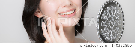 A close-up shot of a young woman checking the condition of her skin by touching it while looking in a hand mirror; her face is obscured, but her mouth, teeth, and lips are visible. A close-up shot of a young woman checking the condition of her skin by touching it while looking in a hand mirror; her face is obscured, but her mouth, teeth, and lips are visible. 140332899