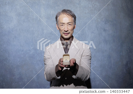 A senior man offers a ring case against a black background. A senior man offers a ring case against a black background. 140333447