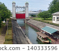 A canal scene with a sluice gate and houseboats lined up. 140333596