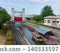 A canal scene with a sluice gate and houseboats lined up. 140333597