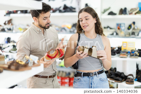 Young woman choosing sandals, her male partner helps at shoe store 140334036