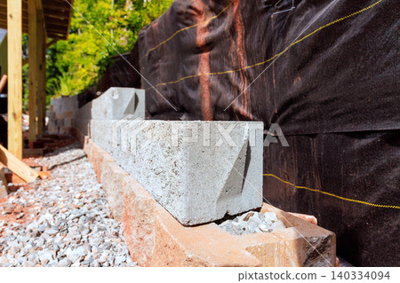 Workers are placing concrete blocks along building foundation surrounded by gravel black tarp 140334094