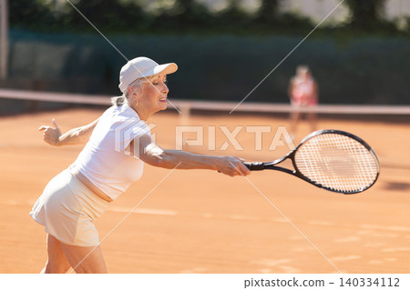 Portrait of emotional active old lady hitting tennis ball with racket on tennis court Portrait of emotional active old lady hitting tennis ball with racket on tennis court 140334112