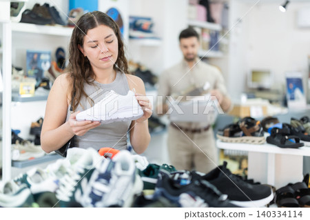 Woman chooses sneakers and a man helps her in the store Woman chooses sneakers and a man helps her in the store 140334114