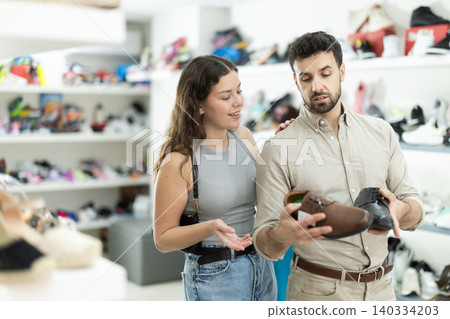 Man chooses classic shoes in shoe store. Young woman helps him with this Man chooses classic shoes in shoe store. Young woman helps him with this 140334203