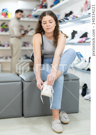 Young woman trying on sneakers at shoe store 140334221
