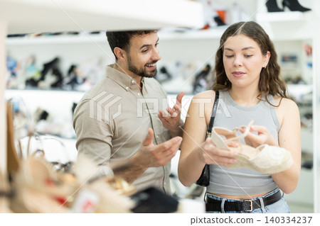 woman stands next to a man who helps her with the choice of shoes woman stands next to a man who helps her with the choice of shoes 140334237