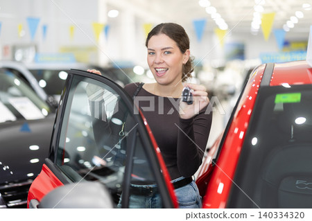 Young woman holding keys to new car in dealership 140334320