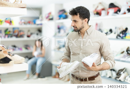 Man shopper in shoe store is looking at sneakers Man shopper in shoe store is looking at sneakers 140334321
