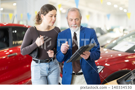 Elderly salesman showing tablet to woman in dealership Elderly salesman showing tablet to woman in dealership 140334530