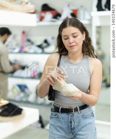Thoughtful woman choosing platform sandals in store Thoughtful woman choosing platform sandals in store 140334679