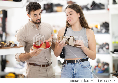Young woman choosing sandals, her male partner helps at shoe store 140334717