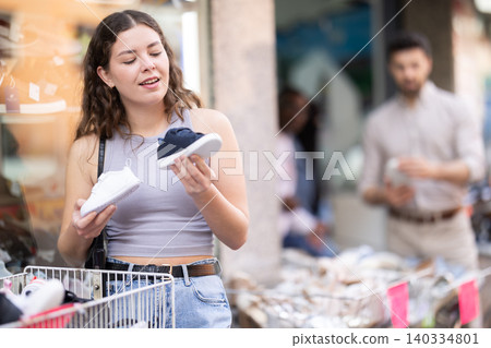 Young woman choosing children's sneakers at outdoor shoe market 140334801